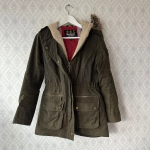 Olivgrön parkajacka från Barbour - Jättesnygg jacka från Barbour. Mjukt teddytyg på insida luva. Kraftigt yttertyg i vaxad bomull. Ngt slitage vid ena ärmslut, se bild. Säljes då den är för liten för mig efter graviditet. Nypris ca 3000kr. Rökfritt hem! Rensar garderoben så se gärna mina andra annonser!