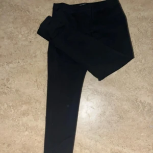 Svarta kostymbyxor från First Class Collection - Snygga svarta kostymbyxor från First Class Collection. De har en klassisk design med dragkedja och knapp framtill. Perfekta för en stilren look.