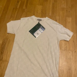 Vit t-shirt från Gucci - Snygg vit t-shirt från Gucci med diskret mönster. Perfekt för en stilren look. T-shirten är kortärmad och har en normal passform. Kommer med originaletiketter från Farfetch.