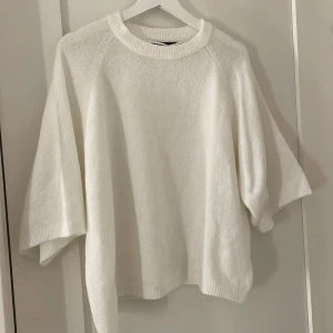 Vit stickad tröja från 157 - Säljer en stilren vit stickad tröja från 157. Tröjan har en avslappnad passform med trekvartsärmar och rund halsringning. Perfekt för kyligare dagar och enkel att matcha med olika outfits.