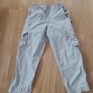 Beige cargobyxor från Walk by Texpak - Säljer ett par beige cargobyxor från Walk by Texpak. Byxorna har flera praktiska fickor och en elastisk midja för extra komfort. Perfekta för en avslappnad stil. Har lite slitningar där olika metallknappar rostat men inget man lägger så stort märke till.!