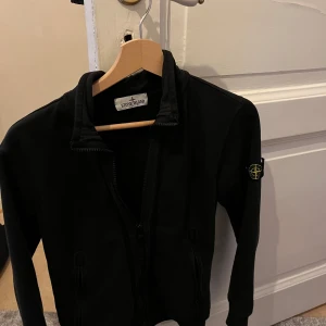 Svart jacka från Stone Island - Säljer denna fina stone Island hoodie. Passar 13-14 åringar, runt 160cm långa. Lite lite missfärgad, men inget som märks. Hör av dig vid minsta lilla fråga