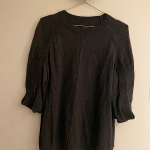 Mörkgrå tröja från AllSaints - Säljer en stilren mörkgrå tröja från AllSaints. Tröjan har trekvartsärmar och en ribbad detalj vid ärmarna och halsen. Perfekt för en avslappnad look.