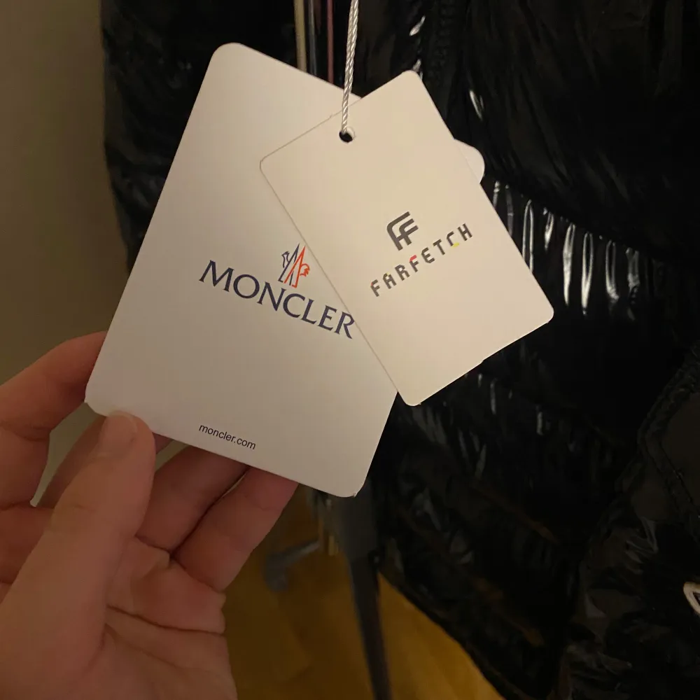 Snygg och glansig svart dunjacka från Moncler med dragkedja och huva. Jackan har en quiltad design och Moncler-logotypen på ärmen. Perfekt för kyliga dagar med stil. Finns från storlek S-XXL. Takit.
