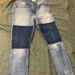 Jeans med lappar - Snygga jeans från tiger of sweden med unika lappar på knäna. De har en klassisk blå tvätt och en straight passform. Perfekta för en avslappnad stil.