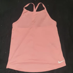 Rosa nike linne - Snygg rosa linne  från Nike med smala axelband och ett stilrent tryck på framsidan. Perfekt för träning eller en avslappnad dag. Tillverkad i ett mjukt och bekvämt material.