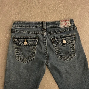 Blå jeans med bootcut - Säljer ett par true religion jeans i storlek W:28 Jeansen har en sliten look med små hål på benen som är en del av designen. Midja:35 Innerbenslängd: Ca 72cm