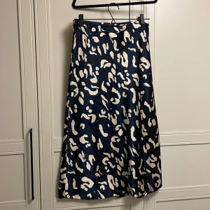 Mörkblå långkjol - 83 cm lång kjol i leopardmönster. Är marinblå med beige/guldigt mönster. Är oanvänd. Är glansigt material. 