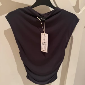 Mörkgrå topp Gina Tricot - Snygg mörkgrå topp med en lite hög krage från Gina Tricot. Perfekt för en stilren look. Helt oanvänd med prislapp kvar! 120kr + frakt