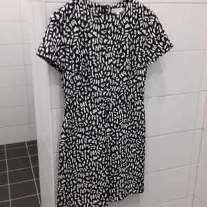 Svart och vit mönstrad klänning från Warehouse - Snygg svart och vit mönstrad klänning från Warehouse. Den har korta ärmar och en rund halsringning. Perfekt för en stilren look.