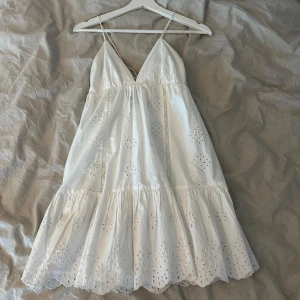 Vit klänning från Zara - Säljer en vacker vit klänning från Zara med broderade detaljer och volang. Klänningen har en v-ringad design och smala axelband med knytning i ryggen. Perfekt för sommarens alla tillfällen!