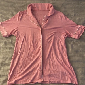 Rosa kortärmad skjorta från Intimissimi - Säljer en mjuk rosa kortärmad pyjamas skjorta från Intimissimi. Skjortan har knappar framtill och vita detaljer längs kragen och ärmsluten. Använd få gånger🌸ordinarie pris 559kr säljer för 320kr. 