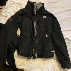 Svart jacka från The North Face - Säljer en svart jacka från The North Face med dragkedja och hög krage. Jackan har långa ärmar och flera praktiska fickor. Perfekt för kyligare väder.