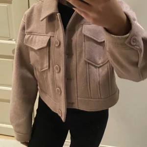 Rosa croppad kappa från NA-KD - Snygg mörkrosa croppad jacka från NA-KD med knappar framtill och två bröstfickor. Jackan har en klassisk krage och långa ärmar, perfekt för en trendig look. Har anvönts fåtal gånger så den är i bra skick. Jackan är i storlek S men passar nog även XS. Kontakta för mer information