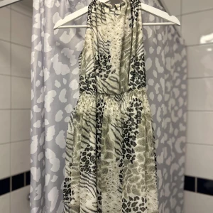 Mönstrad klänning med djurmotiv - Snygg klänning med djurmotiv i svart och beige. Klänningen har en lös passform och är ärmlös, perfekt för en trendig look. Den har ett elastiskt band i midjan för en bekväm passform.