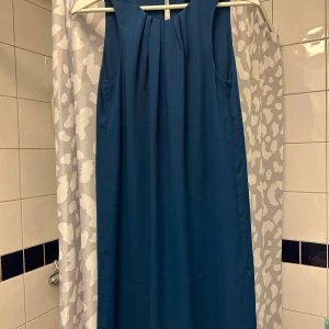Blå ärmlös klänning från H&M - Snygg blå ärmlös klänning från H&M i en elegant och enkel design. Perfekt för både vardag och speciella tillfällen. Klänningen har en stilren look med en liten öppning i ryggen.