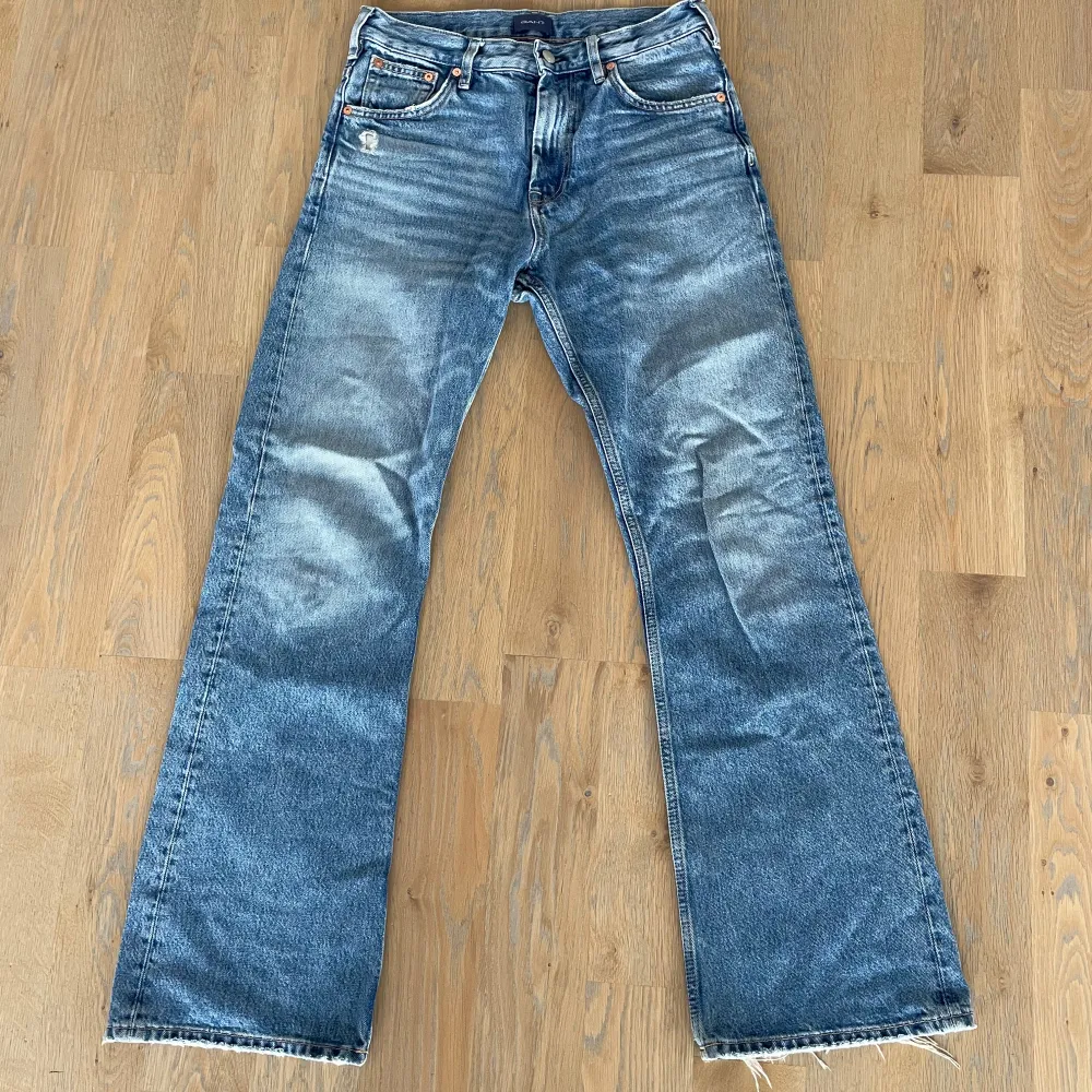 Säljer ett par klassiska blå bootcut jeans med slitna kanter. De har en midwaist passform och är perfekta för en avslappnad stil. Jeansen har fem fickor och en dragkedja med knapp framtill.. Farkut & Housut.