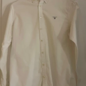 Vit skjorta från GANT - Klassisk vit skjorta från GANT med broderad logga på bröstet. Skjortan har långa ärmar och knappar framtill. Har dock lite fläckar vid armhålorna men det går bort med galltvål. Super bra skick förutom fläckarna