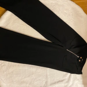 Svarta byxor från Bik Bok - Snygga svarta byxor från Bik Bok med dragkedja och knappar framtill. Byxorna har en stilren design och passar perfekt för en chic look.