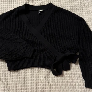 Svart omlott kofta - Snygg svart omlott kofta med ribbad struktur och knytband i midjan. Perfekt för lager-på-lager och ger en stilren look. Långärmad design som passar bra till både vardag och fest. Om ni vill se den på, skriv gärna!