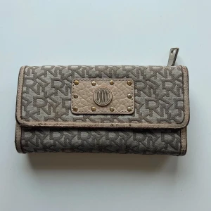 DKNY plånbok - Beige plånbok från DKNY. Längd: 19 cm. Bredd: 10 cm. Bilderna visar skicket