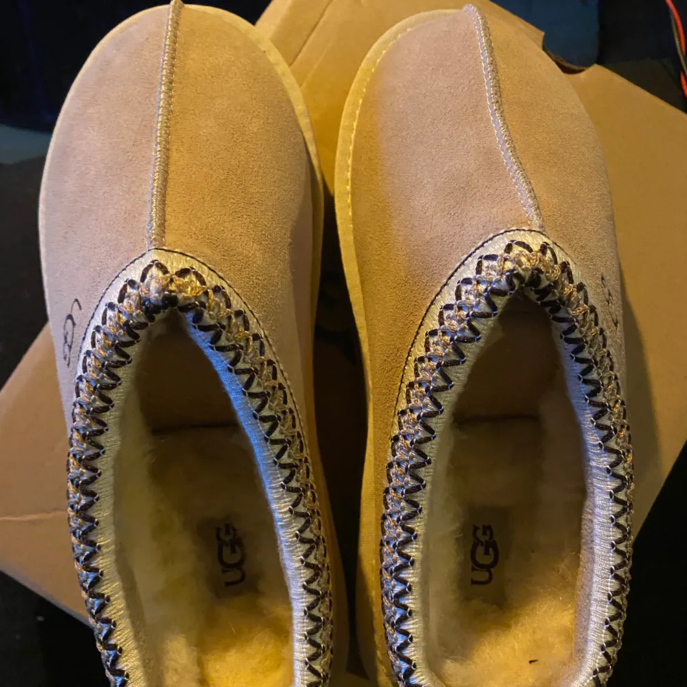 Säljer ett par snygga beige mockaskor från UGG med fluffigt foder och dekorativ söm runt kanten. Skorna har en robust sula och är perfekta för kyligare dagar. De är både stiliga och bekväma.. Kengät.
