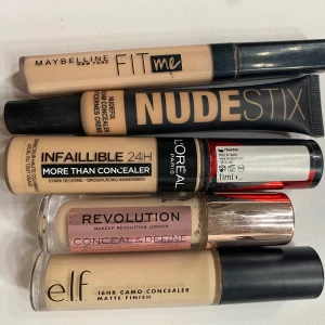 Concealers från olika märken - Samling av concealers från Maybelline Fit Me, Nudestix, L'Oréal Infaillible, Revolution Conceal & Define och e.l.f. 16HR Camo. Nyansvariationer inkluderar Nude 5, Oatmeal, C6.5 och Light Beige. Perfekt för att täcka ojämnheter och ge en jämn hudton. Använts 1-3 ggr