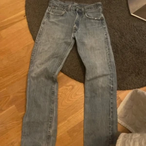 Levis 501 jeans i ljusblå denim - Klassiska Levis 501 jeans i ljusblå denim. De har en rak passform och är midwaist. Jeansen har den ikoniska Levis-lappen bak och en röd etikett på bakfickan. Perfekta för en avslappnad stil. På lappen står 30x34 men dem passar som 28x30 eller 28x32