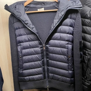 Moncler cardigan - Snygg mörkblå cardigan från Moncler med stickade ärmar och huva. Västen har dragkedja framtill och Moncler-logga på ärmen. Perfekt för kyliga dagar.