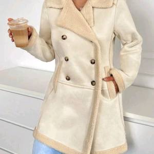 Beige pälsjacka med knappar - Säljer en superfin beige pälsjacka med dubbelknäppning. Den har en mysig och varm känsla med fuskpälsdetaljer på kragen och ärmslute. Perfekt för höst och vinter! Jackan har en normal passform och är långärmad. Den är både stilren och bekväm.