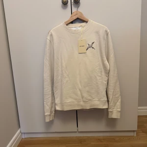 Vit tröja från Axel Arigato - Säljer en stilren vit tröja från Axel Arigato. Den har en snygg broderad fågel på bröstet och är i nyskick. Perfekt för både vardag och fest!