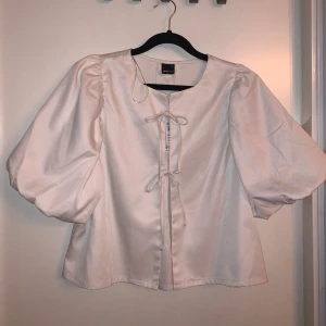 Vit blus från Gina Tricot - Säljer den populära superfina vita blusen från Gina Tricot i storlek M. Blusen har puffiga ärmar och en söt knytning framtill. Helt ny! Nypris är 399kr