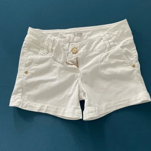 Vita shorts från Staff - Säljer ett par snygga vita shorts från Staff. De har en klassisk design med knappar och dragkedja framtill. Shortsen har fickor både fram och bak, vilket är superpraktiskt. Perfekta för sommardagar eller en avslappnad vårlook. De är i bra skick och redo för nya äventyr!