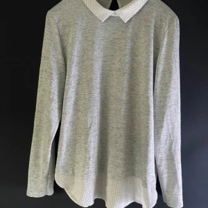 Grå långärmad tröja med prickig krage - Säljer en stilren grå långärmad tröja med en söt prickig krage och nederkant. Perfekt för både vardag och lite finare tillfällen. Den har en liten öppning bak i nacken för extra detalj. Superbekväm och lätt att matcha med andra plagg!