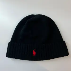 Säljer en snygg svart mössa från Polo Ralph Lauren. Den är stickad och har en röd broderad logga framtill. Perfekt för att hålla sig varm och stilren under de kallare månaderna! Den är lite nopprig på framsidan men annars är den 10/10 skick. 