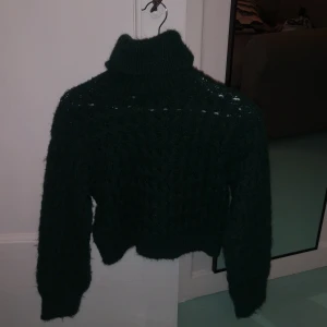 Mörkgrön stickad polotröja - Säljer en supermysig mörkgrön stickad polotröja. Perfekt för kalla dagar med sin höga krage och långa ärmar. Tröjan är croppad och har ett snyggt stickat mönster som ger den en unik look. Passar perfekt till både vardag och mysiga hemmakvällar. 🧶💚