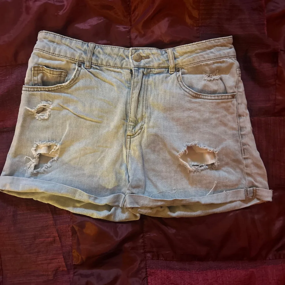 Säljer ett par ljusa jeansshorts med coola slitningar fram och bak. De har en klassisk femficksdesign och är perfekt för en avslappnad sommarlook. Shortsen är i en loose passform och har en bekväm midwaist. Perfekta för festivaler eller en dag på stranden!. Shorts.