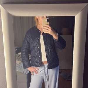 Quiltad jacka i två färger - Säljer en quiltad jacka som finns i både mörkblå och ljusblå färg. Jackan har en enkel design med knappar framtill och långa ärmar. Perfekt för en stilren look.