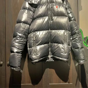Ralph lauren dunjacka - Snygg svart ralph lauren jacka som är lite glansig, köptes 2023 så är lite använd, har kvitto på den, säljer för den är lite stor för mig, har ett litet hål men synd knappast