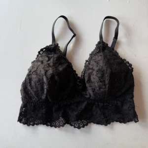 Spets bralette - Snygg svart bralette i spets med justerbara axelband. Den har ett vackert blommigt mönster och en bred spetskant nedtill. Perfekt för att lägga till en touch av elegans till din outfit.