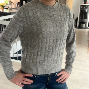 Grå stickad tröja  - Säljer en stilren grå stickad tröja från Divided. Tröjan har ett klassiskt flätmönster och rund halsringning. Perfekt för kyligare dagar. Passar bra till jeans eller kjol. 🧶