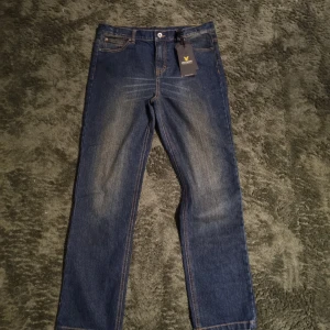 Blå jeans från Lyle and Scott - Snygga blå jeans från Lyle and Scott med klassisk femficksdesign och en diskret tvätt för en trendig look. De har en knapp och dragkedja framtill samt en liten logga på bakfickan.