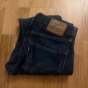 Mörkblå jeans från Levi's 512 - Snygga mörkblå jeans från Levi's med klassisk femficksdesign och en bekväm passform. Perfekta för en stilren look. Levi's logga syns på bakfickan och läderpatchen vid midjan ger en autentisk touch.                                                                Storlek:                                                                               W:32 L:32