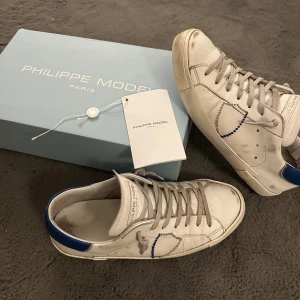 Feta Philippe Model - Feta Philippe Model skor med blå detaljer i storlek 42 men passar storlek 43 också. Skorna är i bra skick förutom att det har en liten defekt i hälen inuti skon men det är inget som syns (kolla sista bilden). Original låda följs med, det är bara att skicka om fler bilder behövs. Går tyvärr inte ner mer i pris.