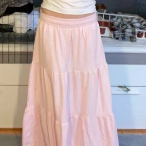 Ljusrosa långkjol - Säljer en ljusrosa fin somrig långkjol med elastisk midja. Kjolen har en luftig och bekväm passform, perfekt för varma dagar. Den är i ett mjukt och lätt material som ger ett fint fall.