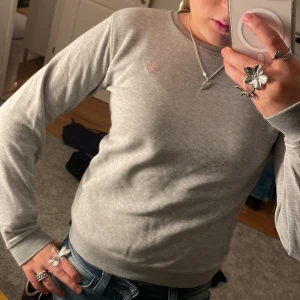 Grå sweatshirt från GANT - Säljer en stilren grå sweatshirt från GANT. Tröjan har en rund halsringning och långa ärmar. Ljusrosa loga och på insidan 