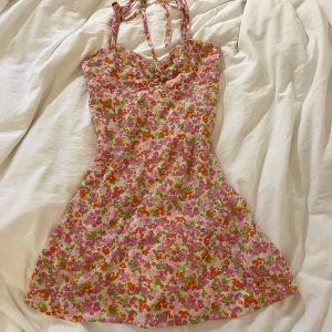 Blommig sommarklänning - Söt blommig klänning i rosa, grön och orange. Dragkedja på baksidan och banden går att justera. Klänningen har en smickrande passform och ärmlös design.
