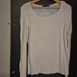 Vit långärmad topp från Åhléns - Säljer en stilren vit långärmad topp från Åhléns. Perfekt basplagg med rund halsringning, tillverkad i mjukt material för bekväm passform. Passar utmärkt till lager-på-lager eller som den är.