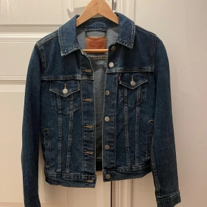 Jeansjacka från Levi’s - Säljer en klassisk jeansjacka från Levi’s. i mörkblå denim. Jackan har en normal passform med knappar framtill och två bröstfickor med knappstängning. Använd en gång.