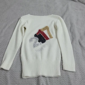 Vit stickad tröja med mönster - Säljer en vit stickad tröja med ett färgglatt mönster på framsidan. Tröjan har långa ärmar och ribbstickade muddar vid ärmslut och nederkant. Perfekt för kyligare dagar.